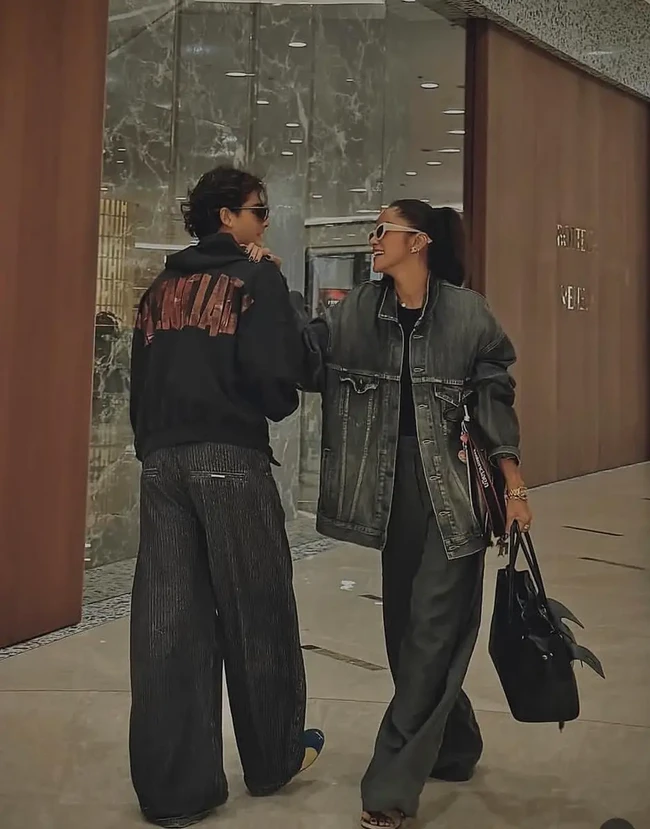 Olla memadukan jaket denim oversized dengan celana palazzo abu-abu gelap, kacamata hitam berbingkai putih, dan tas kulit hitam. Tristan tampil tak kalah keren dengan hoodie hitam beraksen grafis merah serta celana panjang longgar bermotif garis. Perpaduan tersebut menghadirkan gaya streetwear yang modern dan kekinian. Foto: Instagram/@ollaramlan
