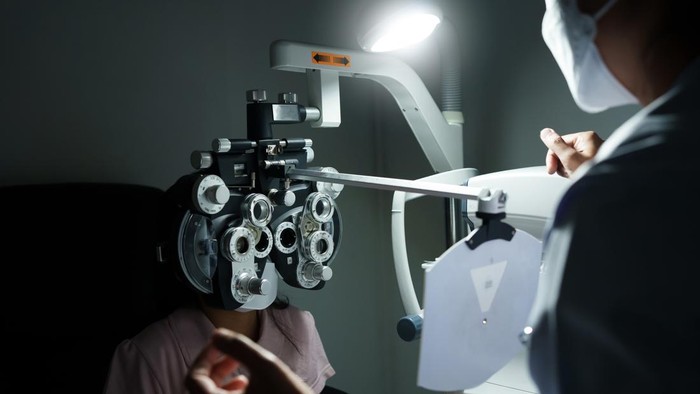 Ophthalmologist examining the eyes of an Asian girl in a clinic. They wear protective face masks.