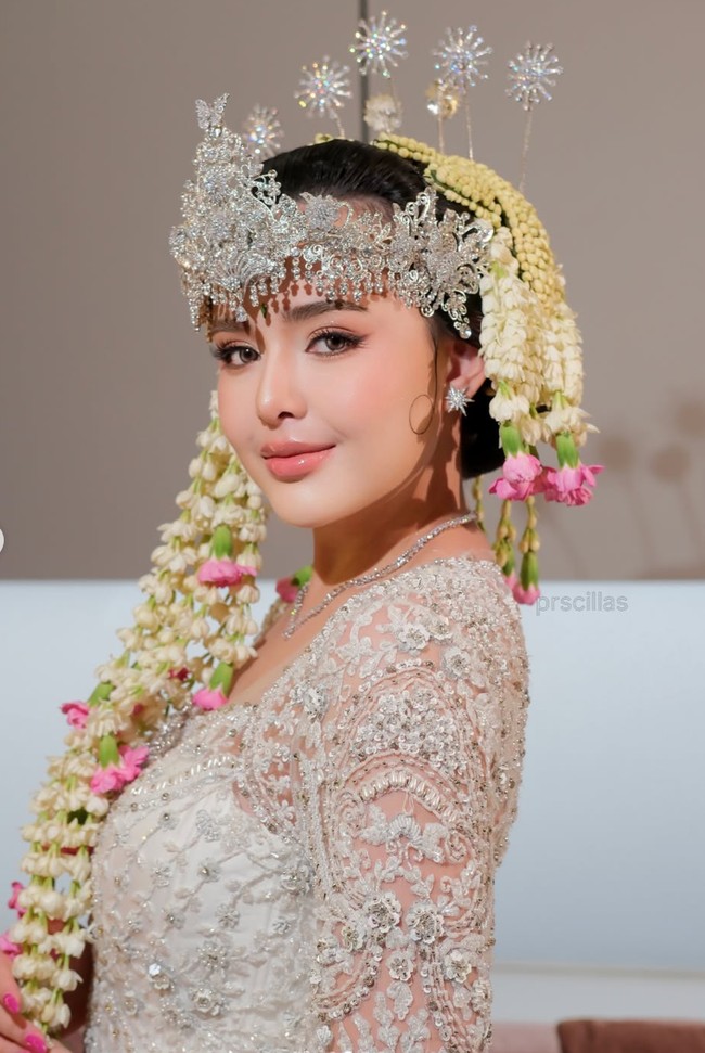 Bagian leher kebaya memiliki potongan persegi yang memperlihatkan area tulang selangka. Model ini memberikan kesan anggun sekaligus modern pada busana pengantin tradisional. Kebaya tersebut juga memiliki lengan panjang berbahan transparan dengan hiasan bordir dan payet senada. Foto: Instagram/@prscillas