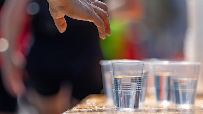 hand of a marathon runner reaches for plastic cup with water