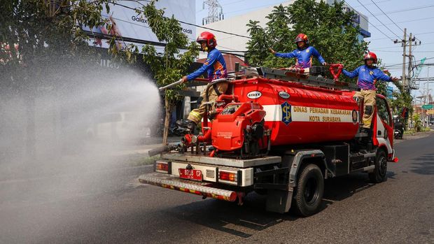 Petugas Damkar menyemprot jalanan di Surabaya demi mengatasi panas dan debu proyek yang bikin warga beraktivitas tidak nyaman.