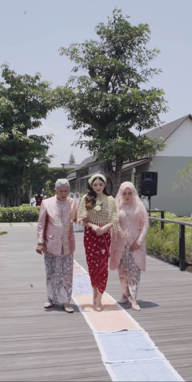 Untuk prosesi siraman, Yuriska kembali beerganti pakaian dengan mengenakan kain lilit jumputan berwarna merah. Penampilannya juga ssemakin lengkap dengan cape ronce melati.&nbsp;Foto: Instagram/@bumitarate