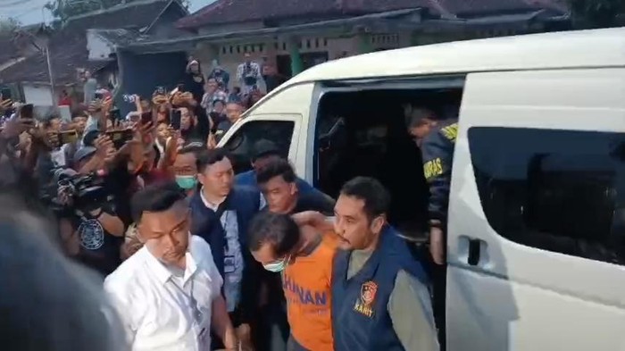 Dwi Bagus (kaus tahanan oranye) disoraki dan dimaki warga saat menuju rumah keluarganya untuk rekonstruksi di Kota Madiun