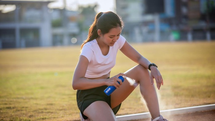 Asian Sports women using freezing spray for treating injured sportwomens knee and leg after run