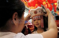 Seorang ibu sedang mencoba topi Imlek untuk anaknya.