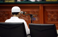 Umar Patek mendengarkan dakwaan JPU dalam persidangan perdananya. Ia menggunakan busana gamis dan peci berwarna putih.