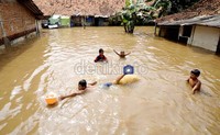 Beberapa anak bermain di halaman rumahnya yang terendam banjir.