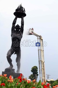 Petugas membersihkan bagian atas patung menggunakan tangga yang bisa ditinggikan.