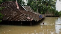 Seorang warga berenang untuk memeriksa kondisi rumahnya yang nyaris tenggelam karena genangan air.