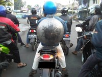Pengendara motor bernomor polisi B ini dengan santai mengendarai motor sambil membawa wajan di punggungnya.