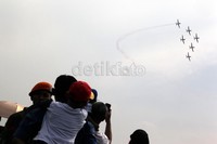 Soerang anak digendong orangtuanya, menyaksikan atraksi pesawat yang membentuk formasi.