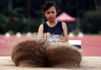 Atlet junior putri, berusaha tampil terbaik dalam lompat jangkit di tengah pasir yang berhamburan.