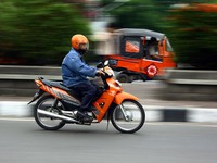 Seorang sopir bajaj dan Pak Pos sedang melaju beriringan di dua sisi jalan. Sehingga terlihat keduanya seperti sedang balapan.