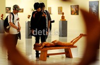 Pengunjung pameran memperhatikan patung perempuan tengkurap tanpa busana.