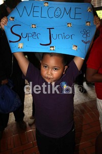 Tak hanya remaja, tampak seorang anak kecil dengan mengenakan busana berwarna ungu dan membawa spanduk penyambutan selamat datang kepada SuJu.