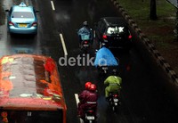 Seorang pengendara sepeda motor menerobos hujan dengan menggunakan jas hujan jenis ponco.