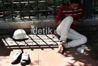 Seorang buruh, tengah bersandar di pagar dan asyik ber-SMS.