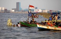Para nelayan beriringan melepas sesaji yang diletakkan di sebuah perahu.