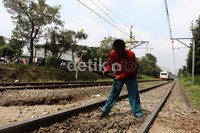 Para pekerja menggeruk batu yang menutupi rel kereta api yang digunakan sebagai perlintasan sepeda motor.