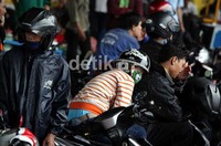 Seorang wanita tengah tertidur diatas kendaraan motornya saat menunggu hujan reda.