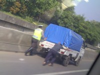 Seorang petugas polisi terlihat tengah membantu mendorong mobil pikap yang mogok di jalan tol (Foto Benny Gunawan).