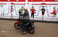 Seorang pengendara motor berhenti sesaat, melihat banner para pemain legendaris bulutangkis Indonesia di Istora Senayan, Jakarta