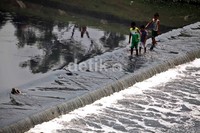Tiga orang anak bermain air di aliran sungai Banjir Kanal Timur, Jakarta.