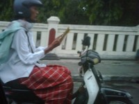 Mengendarai motor, lengkap dengan sarung, dan baju koko.