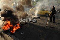 Salah seorang staf pengamanan kampus UMI berupaya memadamkan kobaran api dari ban bekas yang dibakar mahasiswa. Muhammad Nur Abdurrahman/detikcom.