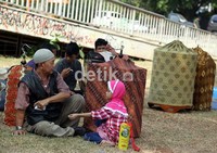 Seorang Kakek bersama cucunya, menunggu perlobaan burung berkicau dimulai di samping sangkar-sangkar burung yang ditutup kain.