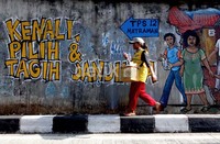 Warga melintas di depan mural di Jalan Salemba, Matraman, Jakarta, Senin (2/7/2012). Pilkada kali ini diikuti 6 pasang calon termasuk incumbent Fauzi Bowo. Selain politik uang, kisruh Daftar Pemilih Tetap (DPT) kerap dipertanyakan kualitasnya.