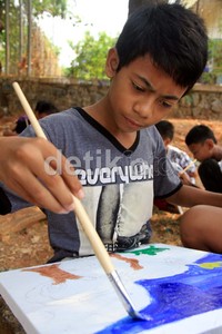 Seorang anak tampak serius melukis.