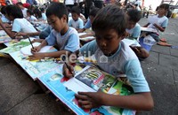 Seorang anak jalanan tampak sedang bersungguh-sungguh mengerjakan soal ujian yang diberikan.