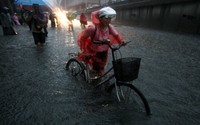 Seorang warga mendorong sepedanya melintasi jalanan yang tergenang banjir di Beijing. Reuters/China Daily.