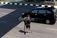 Seorang pengemis tua yang cacat fisiknya menyeberangi jalan utama Kota Bekasi.