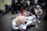 Warga yang mengajak anak-anaknya duduk dengan beralaskan koran sambil mengisi formulir pendaftaran.