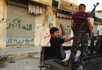 Milisi melakukan patroli di Attarib, Provinsi Aleppo. Dibelakangnya, grafiti bertuliskan Allahu Akbar terlihat.