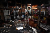 Seorang warga menyiram api yang masih terlihat di puing bekas kebakaran.