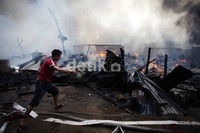 Seorang warga menyiram titik-titik api menggunakan peralatan seadanya.