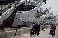 Beberapa wisatawan menggowes sepedanya di depan kapal-kapal yang bersandar.