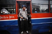 Polisi berjaga di depan metromini yang membawa para tersangka dengan senjata laras panjang.