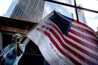 Seorang warga membawa bendera AS yang telah diberi nama-nama korban 911 di area Ground Zero WTC New York.  Hingga detik ini, cerita dibalik peristiwa tersebut masih menyisakan berbagai versi. (Photo by Spencer Platt/Getty Images)
