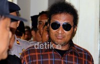 Memakai kaca mata hitam, John Kei tampak santai memasuki ruang sidang.