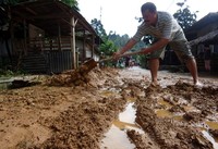 Seorang warga membersihkan jalan yang penuh lumpur. (Rino Zulyadi)