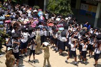 Para siswa berkumpul di halaman sekolah sambil menutupi kepalanya dengan tas.