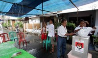 Petugas KPPS berusaha menutup kotak suara dengan plastik. Dibelakangnya, warga berusaha menghalau air hujan yang tergenang di tenda terpal.
