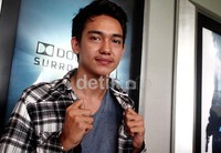 Ia tampak memakai kaos abu-abu yang dipadukan dengan kemeja kotak-kotaknya.