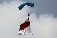 Seorang penerjun payung mengibarkan bendera merah putih.
