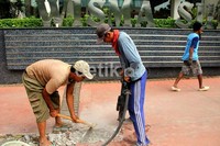Dua orang pekerja membongkar beton jalur pedestrian yang rusak.