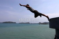 Seorang pemuda melakukan atraksi terjun dari atas kapal.